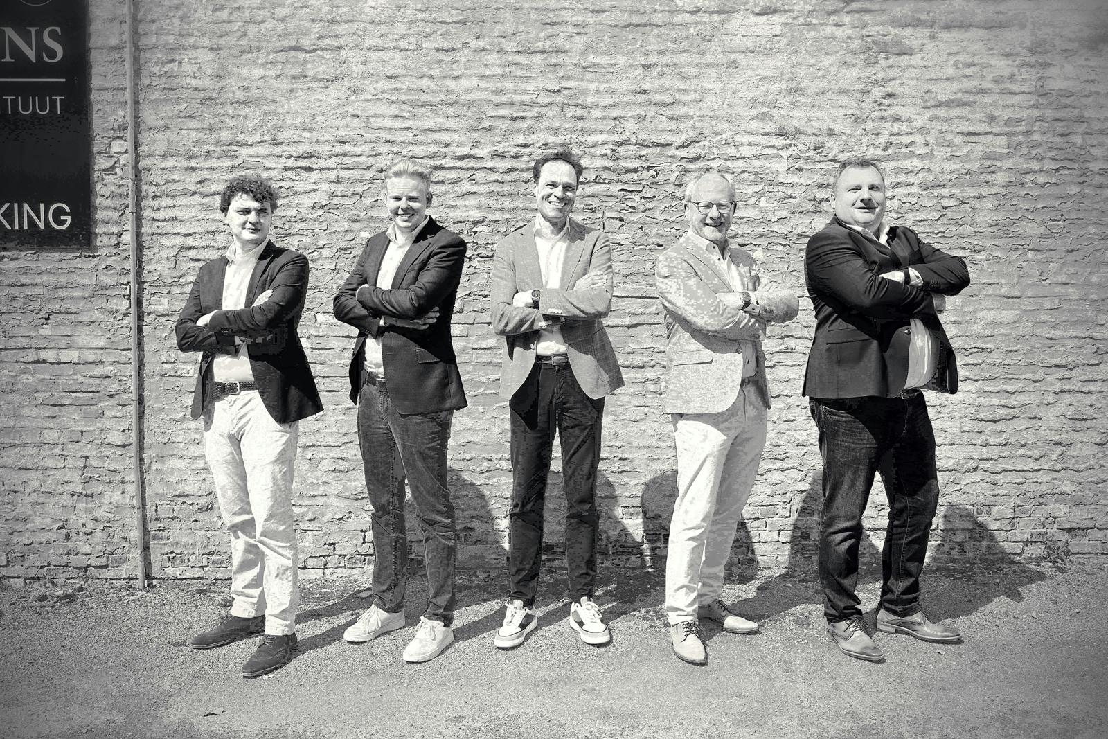 Five men standing together in front of a brick wall